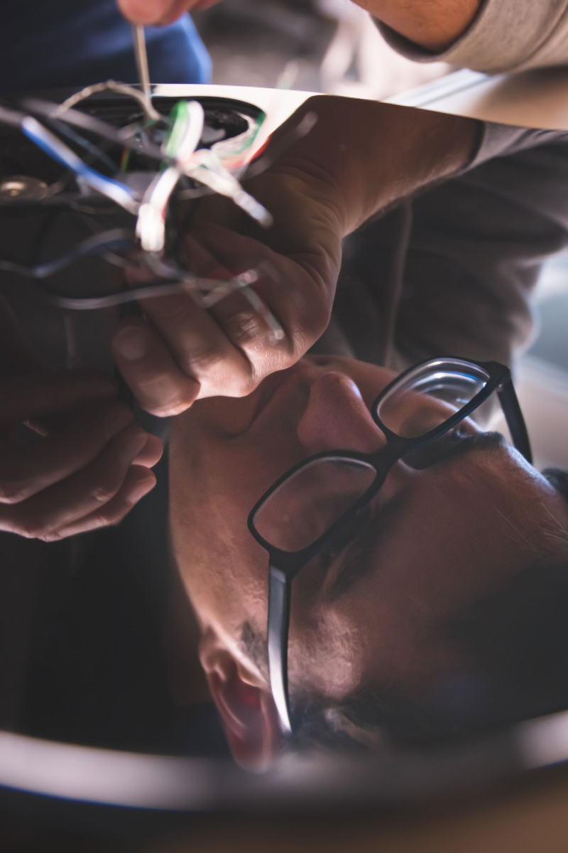 The reflection is shown in the body of a polished guitar. The reflection shows a man doing wiring work on the guitar.