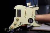 A mint green loaded HSS pickguard with aged white knobs an pickup covers. The pickguard is held aloft by an arm.